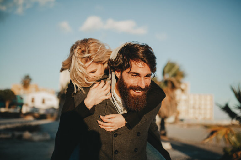 Cool indie couple having fun outdoors while he gives her a piggyback